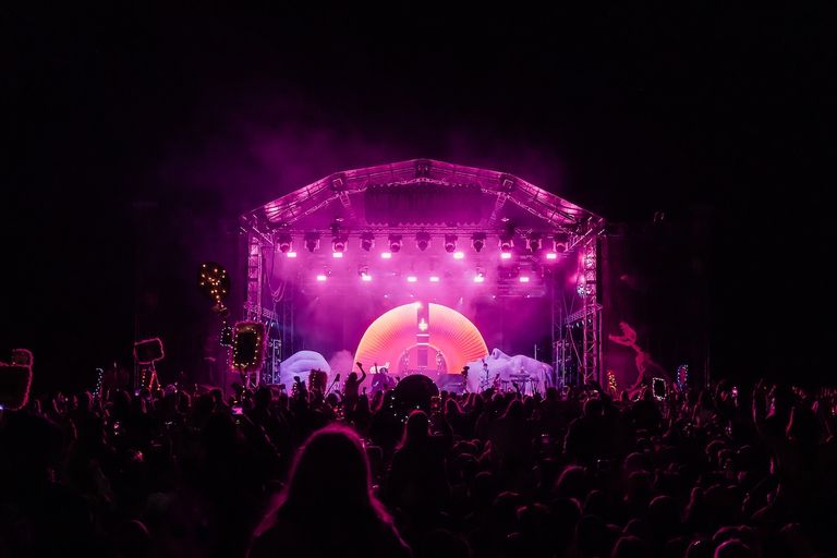 Nighttime crowd at Party in the Paddock festival watching a performance on a brightly lit pink stage.